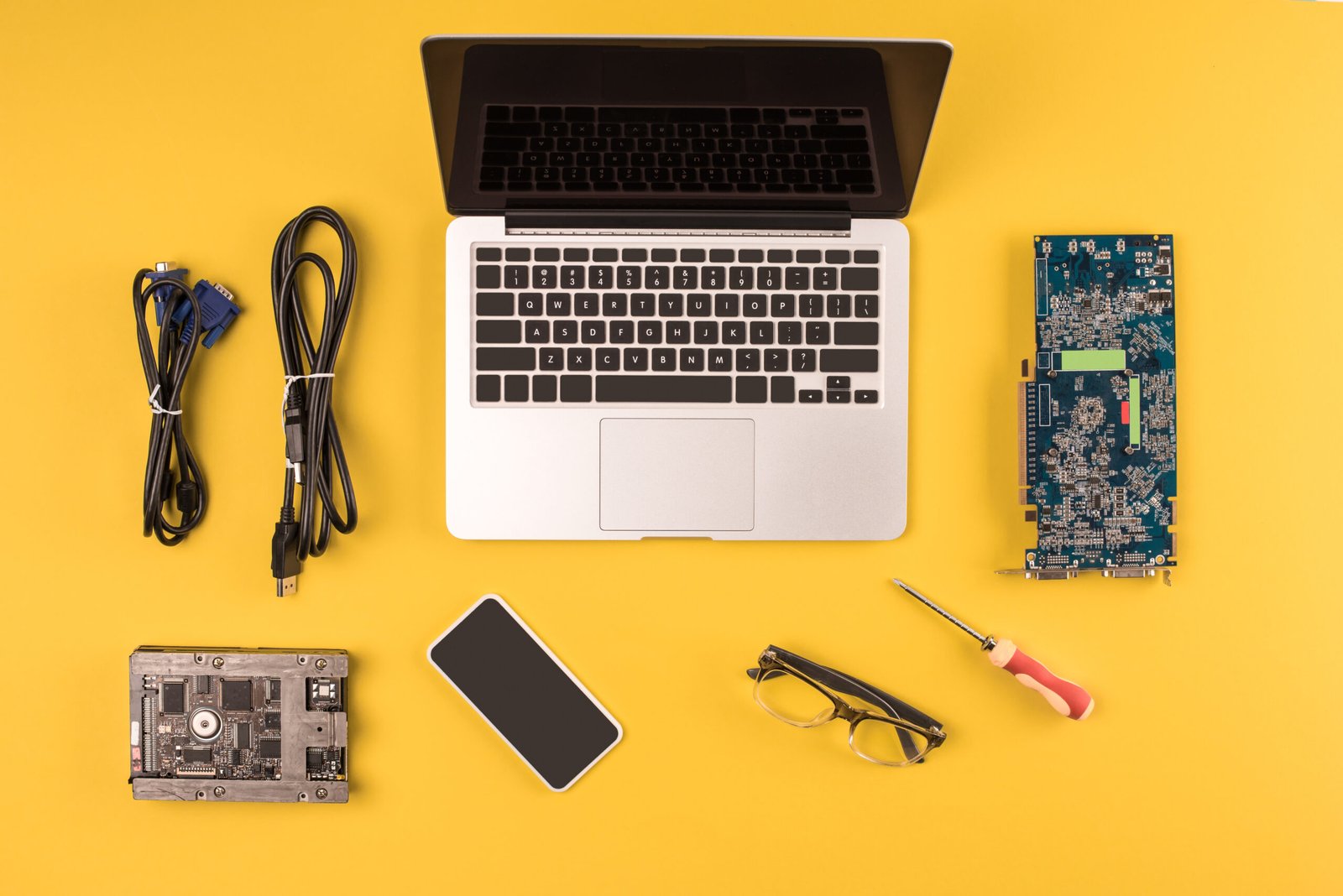 top view of laptop, smartphone, eyeglasses and wires on yellow